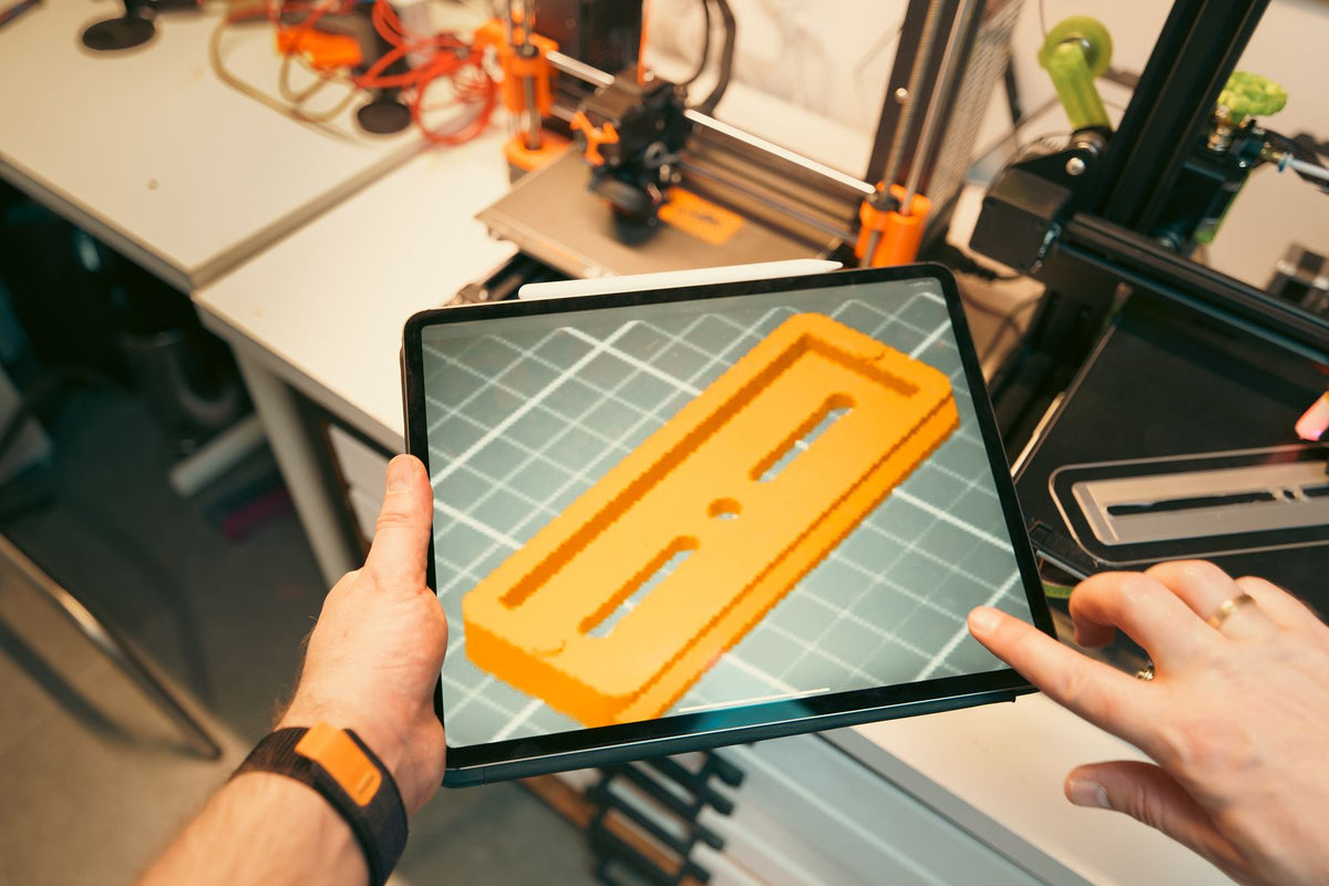 Twee mensen bekijken een 3D ontwerp op een tablet, met een printer op de achtergrond