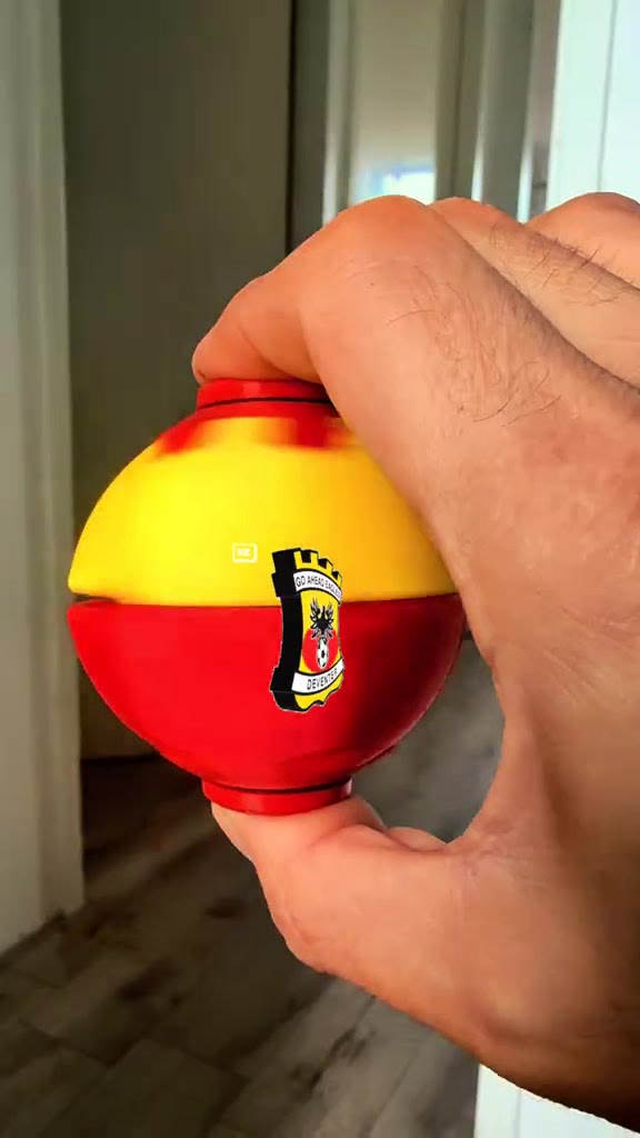 Een 3D geprinte bal in geel en rood met een clubwapen, in een hand
